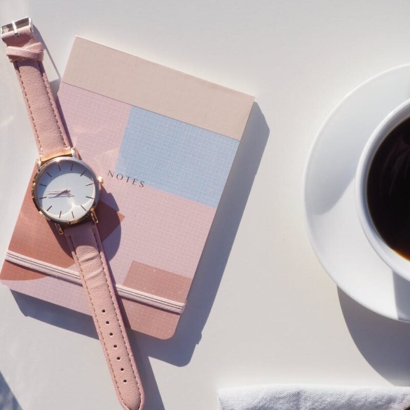 round gold colored analog watch with pink leather strap on pink notebook