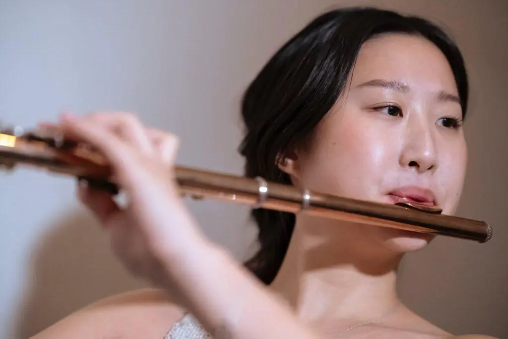 Woman playing the flute with focused expression, highlighting the artistic and expressive nature of music. This image represents the elegance and creativity involved in playing musical instruments, a cherished feminine hobby.