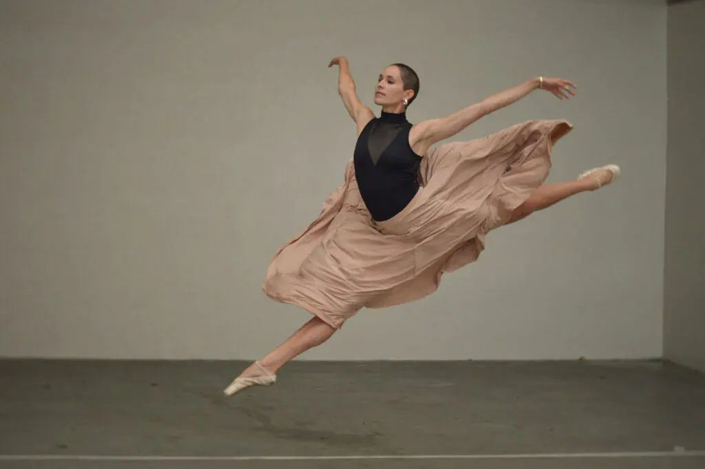 Ballerina performing a graceful leap in a beige flowing skirt and black top, showcasing elegance and poise. This image of a ballet dancer embodies the grace and strength often associated with feminine hobbies.