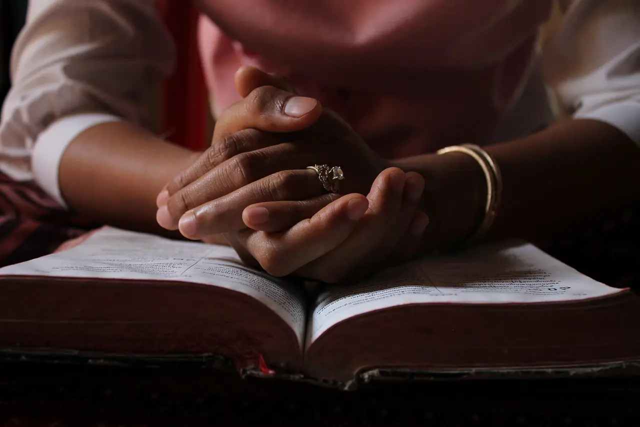 Close-up of a woman's hands clasped together in prayer over an open Bible, highlighting a sense of reflection and spirituality. This image symbolizes the theme of faith and surrender, pertinent to discussions on letting go and letting God verses.