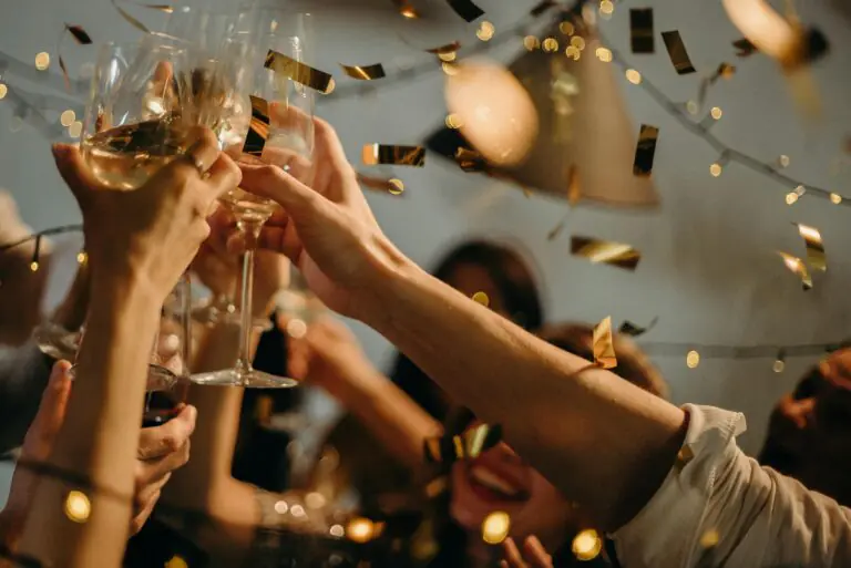 People raising glasses in celebration, surrounded by golden confetti and warm string lights, creating a festive and joyful atmosphere.