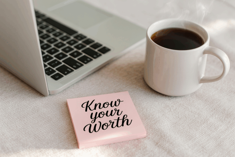 A light pink sticky note with bold black cursive text reading “Know your Worth” rests beside a laptop keyboard and a steaming white mug of coffee on a soft beige surface. The scene evokes a calm, motivational workspace vibe.